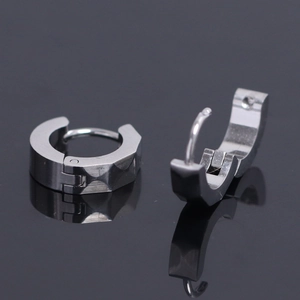 Détail de boucles d'oreilles en acier mat avec une surface facettée géométrique diamantée