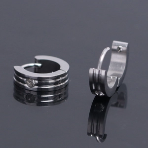 Détail de boucles d'oreilles en acier argenté avec texture rainurée et zircon central