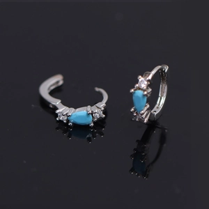 Macro detail of silver hoop earrings with teardrop blue stone and zircon on reflective surface