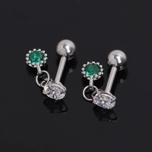 Détail de clous d'oreilles argentés avec zircon vert et cristal sur fond noir réfléchissant