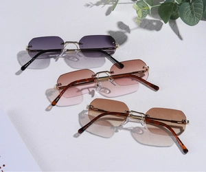 Three rimless octagon sunglasses with gradient lenses and gold metal frames on white stone