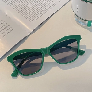 Green geometric square sunglasses with dark grey UV lenses on a white desk