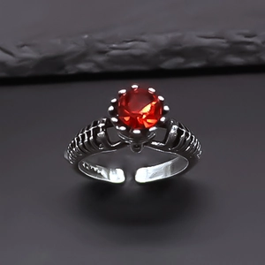 Macro view of gothic skull claw ring featuring a round red faceted stone in antique silver