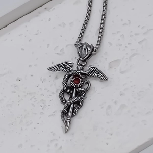 Vintage silver caduceus necklace with double snakes and a red gemstone on marble surface