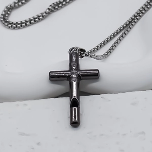 Macro detail of gun-metal stainless steel cross whistle pendant with box chain on stone