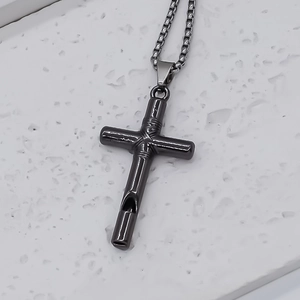 Macro detail of gunmetal cross whistle pendant necklace with box chain on stone base