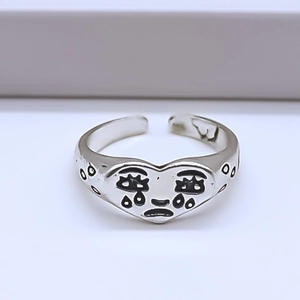 Macro detail of silver heart ring featuring a black crying face graphic in punk style