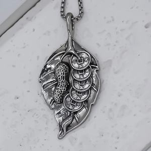 Detailed close-up of leaf pendant with silver peanut and copper coins on metal chain