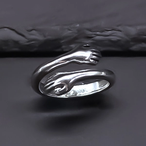 Gros plan d'une bague design mains qui s'enlacent argentée sur fond de pierre texturée