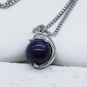 Macro detail of silver dolphin pendant with purple bead on a sleek box chain necklace