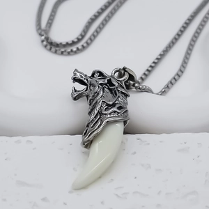 Close-up of a carved silver wolf head pendant with a white curved tooth on a white display