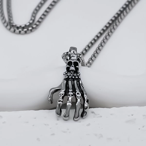 Detailed close-up of gothic skull hand pendant on box chain over white stone texture