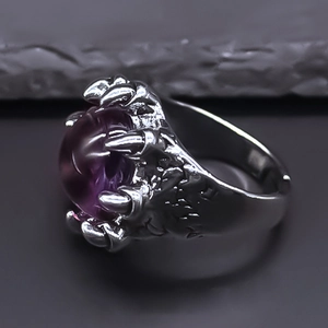 Vue macro d'une bague griffe argentée punk avec une pierre œil de démon violette
