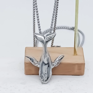 Minimalist silver whale pendant necklace featuring a polished box chain on a wooden display