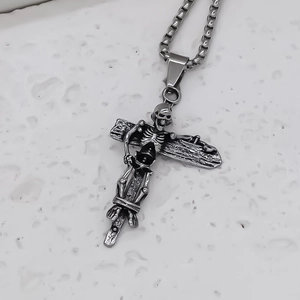 Gothic cross necklace with skull relief in antique silver finish on marble surface