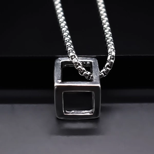 Dettaglio di un ciondolo a cubo geometrico cavo con catena box argento su sfondo nero