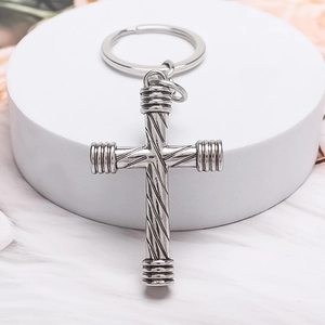 Vintage silver metal cross keychain with spiral texture on a white velvet surface