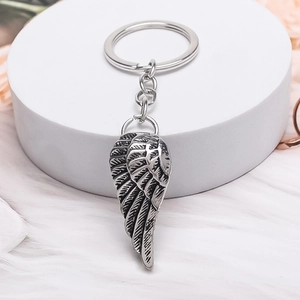 Vintage silver angel wing keychain accessory on a soft white plush background