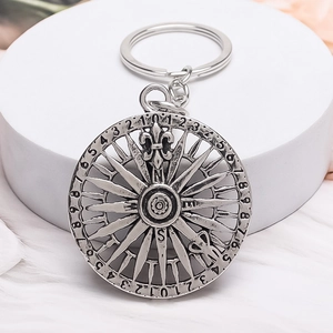 Vintage silver compass keychain with fleur-de-lis pattern on a white pedestal