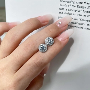Close-up of S925 silver halo stud earrings with sparkling zircon stones on a finger