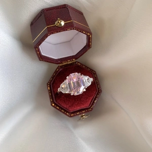 Macro detail of emerald-cut pink gemstone ring with trapezoid accents in red velvet box