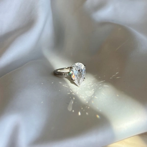 Macro shot of pear-shaped teardrop diamond ring with micro-pave band on white silk