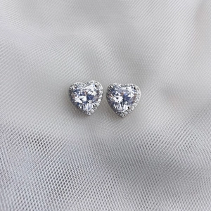 Vue macro de boucles d'oreilles cœur en argent 925 avec zircons sur tulle blanc délicat