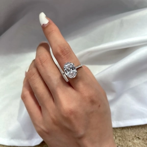 Close-up of oval-cut zircon engagement ring with pavé diamond band on hand