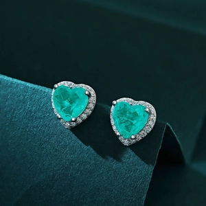 Détail macro de boucles d'oreilles cœur en argent S925 avec zircon émeraude sur fond vert