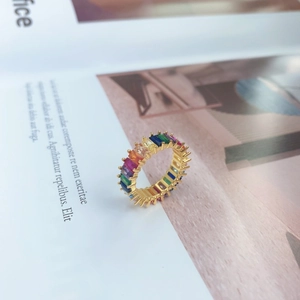 Close-up of gold eternity ring with baguette-cut multi-colored stones on a white magazine