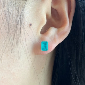Close-up of emerald cut teal gemstone stud earrings worn on ear in silver setting