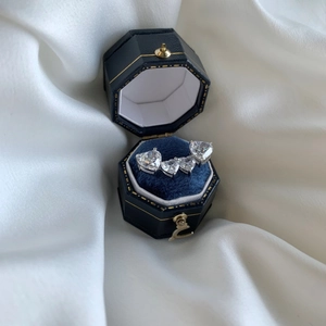 Macro shot of silver heart earrings with four clear zircons in a navy blue velvet jewelry box