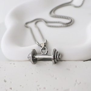 Gros plan d'un collier pendentif haltère en acier argenté sur des pierres texturées blanches