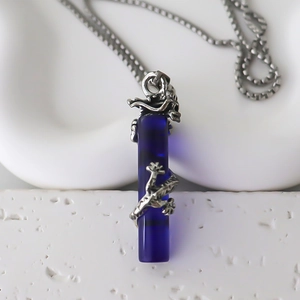 Gros plan du pendentif cylindre en résine bleue avec dragon argenté sur une chaîne