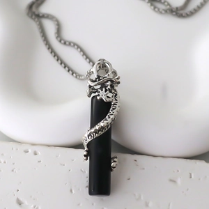 Macro shot of silver dragon winding around a polished black cylinder pendant necklace