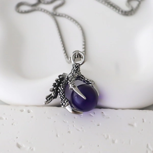 Macro detail of gothic dragon claw pendant with a purple crystal ball and silver chain