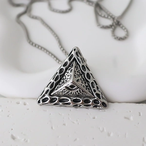 Macro detail of silver pyramid pendant with eye symbol on textured stone background