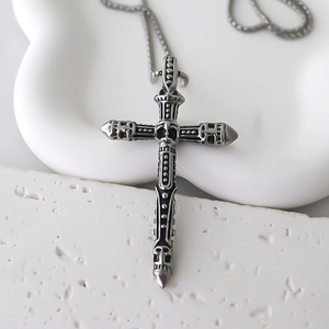 Détail d'un pendentif croix gothique en argent avec crânes sculptés sur un support blanc