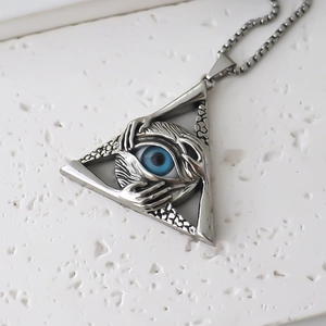 Macro detail of gothic triangle pendant with blue eye and engraved hand on stone base
