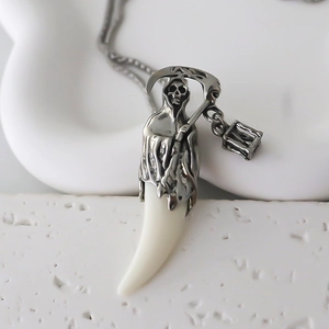 Détail du pendentif Grim Reaper en argent avec une dent blanche sur un support minimaliste