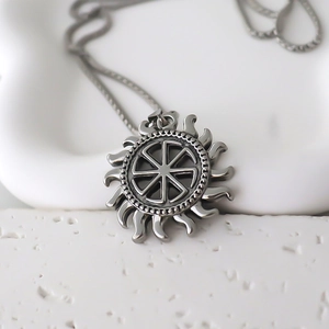 Macro d'un pendentif soleil argenté avec symbole Kolovrat sur support minimaliste