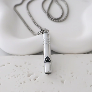 Gros plan d'un pendentif sifflet argenté minimaliste sur une fine chaîne métallique