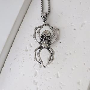 Gothic silver spider skull pendant necklace with matching chain on white stone surface