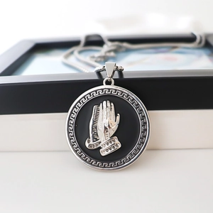 Polished silver alloy necklace featuring a round prayer hands pendant with Greek key borders