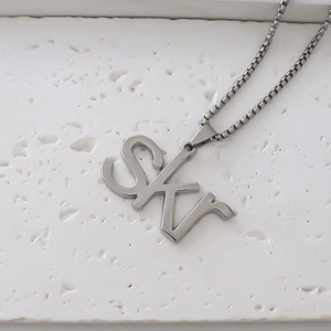 Primer plano del collar con colgante de letra SKR y cadena box plata sobre piedra