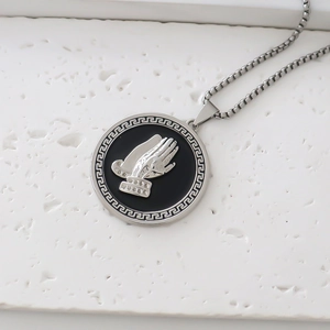 Detailed close-up of a religious round pendant with praying hands and Greek key border