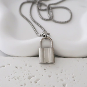 Close-up of a silver padlock pendant on a square link chain resting on a white tray