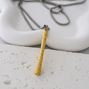 Macro detail of golden staff pendant with cloud pattern relief and box chain