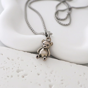 Gros plan du collier avec pendentif ours en argent poli sur une base texturée blanche