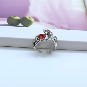 Detail of silver punk ring featuring a figure holding a red gemstone on white stand